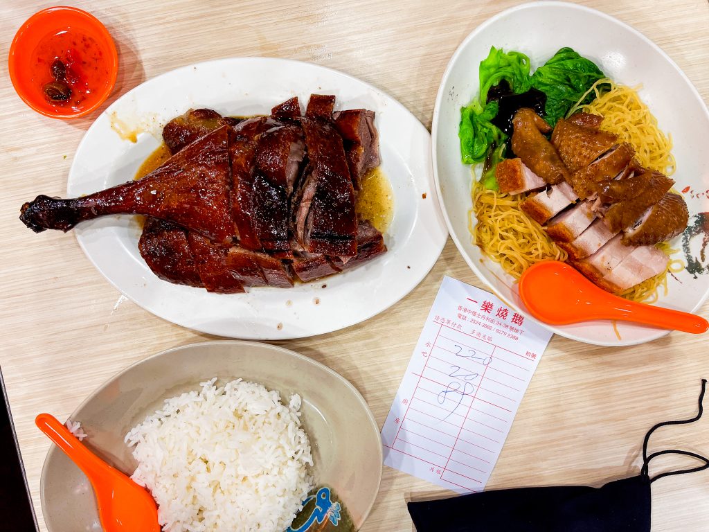 Roast duck, noodle dish with greens and sliced meat, and a bowl of white rice on a table with a receipt nearby.