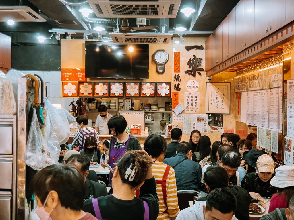 A crowded restaurant with people dining on some of the best food in Hong Kong; walls adorned with menus and posters.