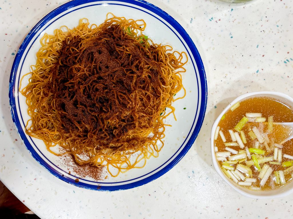 A plate of seasoned noodles with a bowl of broth, garnished with sliced green onions.