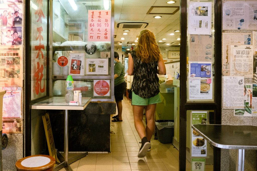 Person with long hair entering a restaurant with various posters and Michelin signs on the walls, indicating some of the best food in Hong Kong.