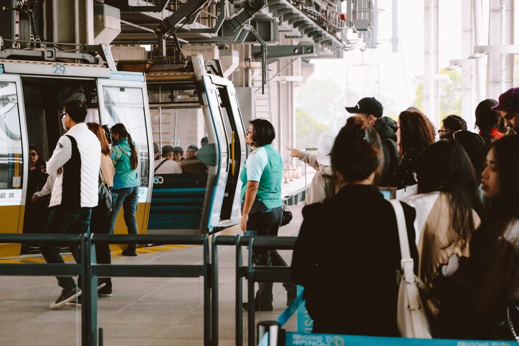 People queue at a cable car station as a uniformed staff member assists in boarding.