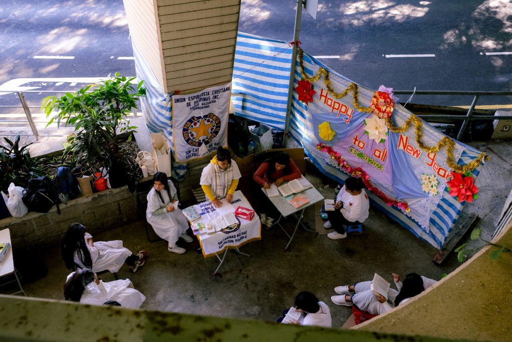 Outdoor health checkup camp with people in white coats, tables with medical supplies. Happy New Year banner above.