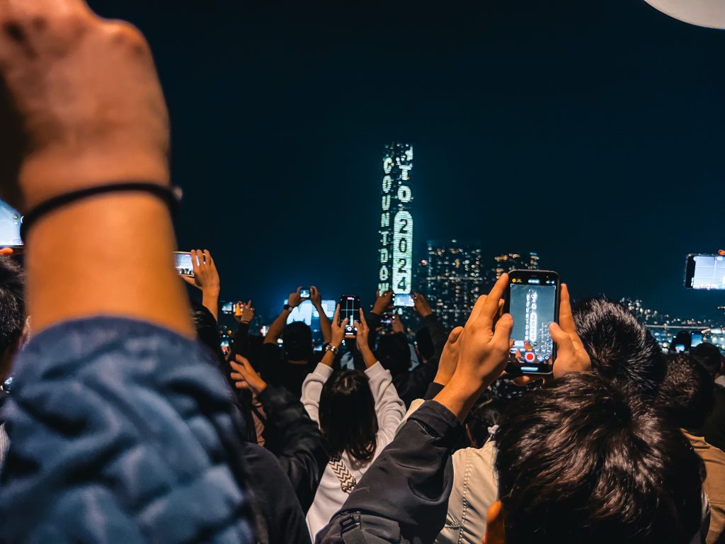 A crowd holds up phones photographing a building displaying Countdown to 2024 on New Years Eve in Hong Kong.