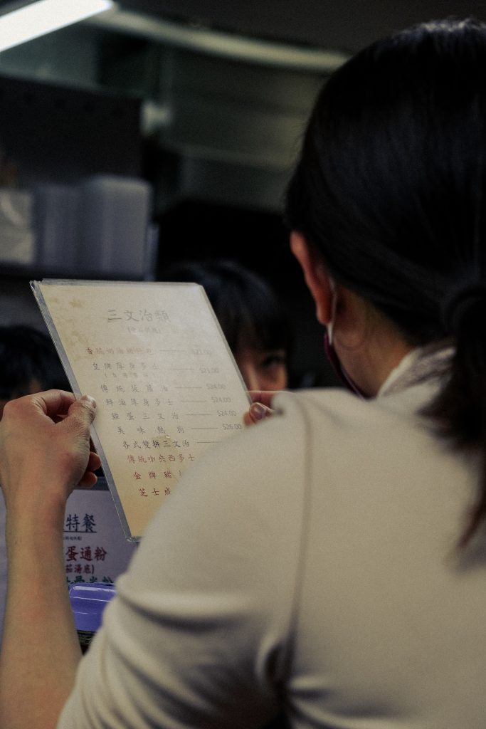 Person reading a menu in a restaurant, with another person visible in the background.