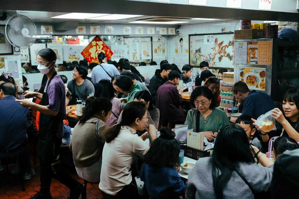 A bustling restaurant with people dining and waitstaff serving, featuring traditional Asian decorations on the walls.