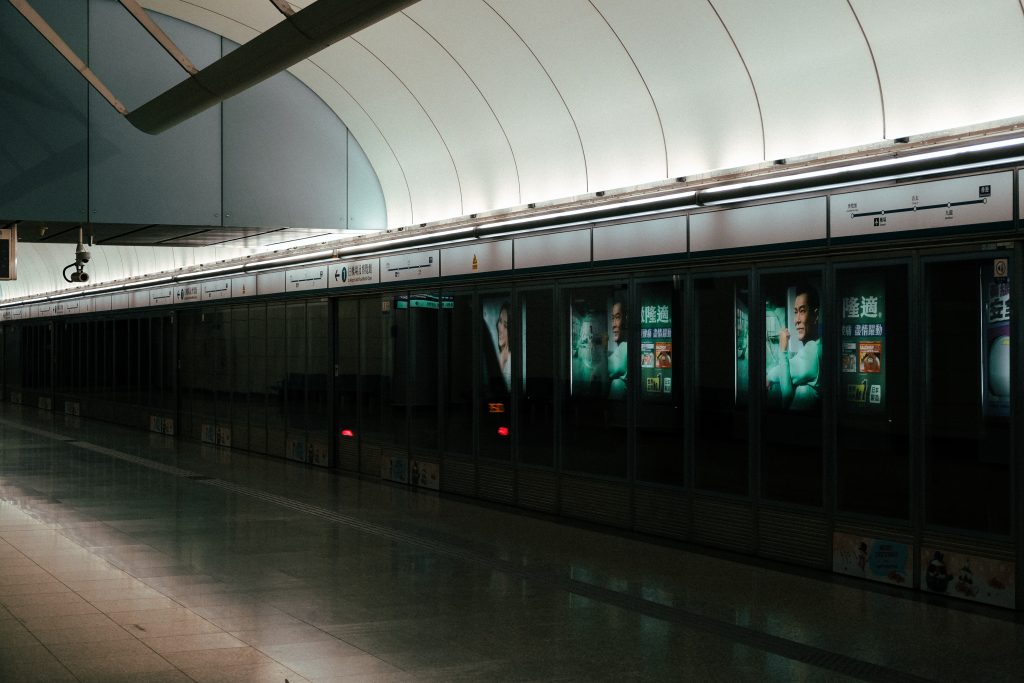 Empty train platform with illuminated advertisements on closed glass doors under a curved ceiling.