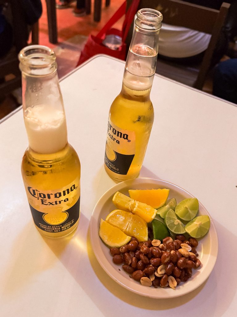Two Corona beers on a table, with a plate of lime, orange slices, and peanuts.