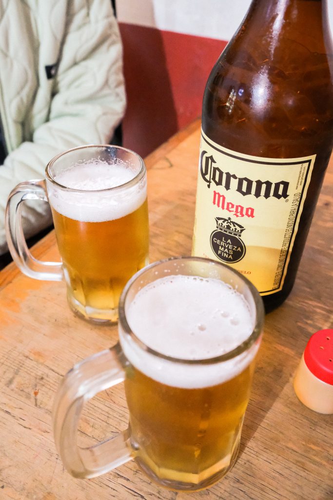 Two beer mugs next to a big Corona Mega beer on a wooden table.