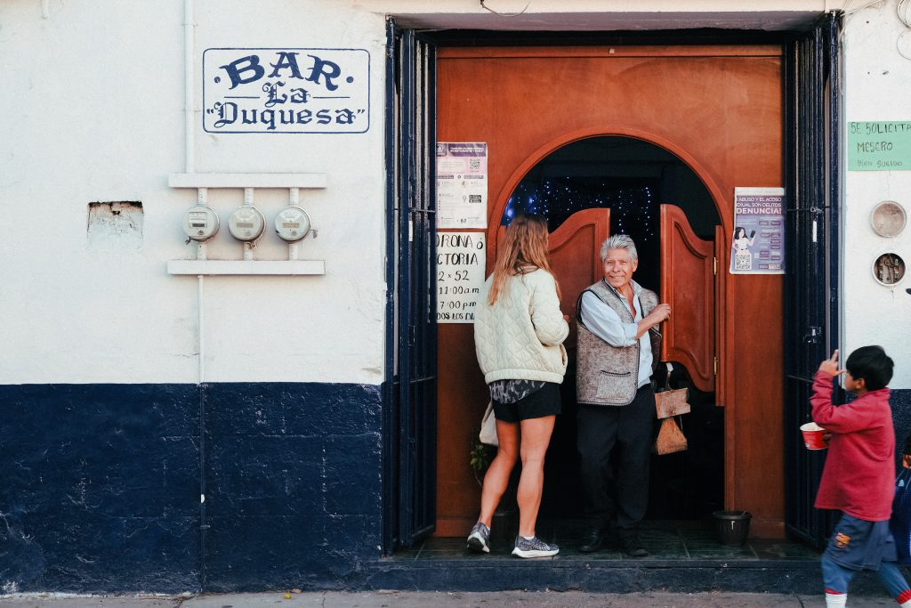 Two people converse at the entrance of Bar La Duquesa as a child holds a drink nearby.
