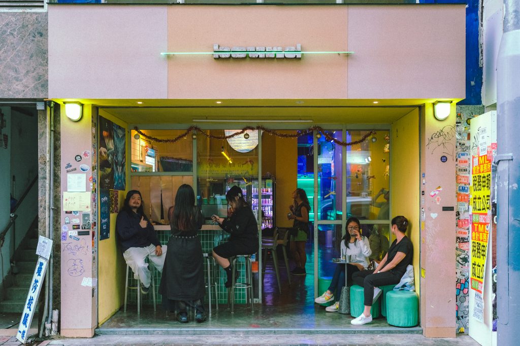 People sitting at a cozy, colorful bar with neon lights and vibrant posters on the walls.