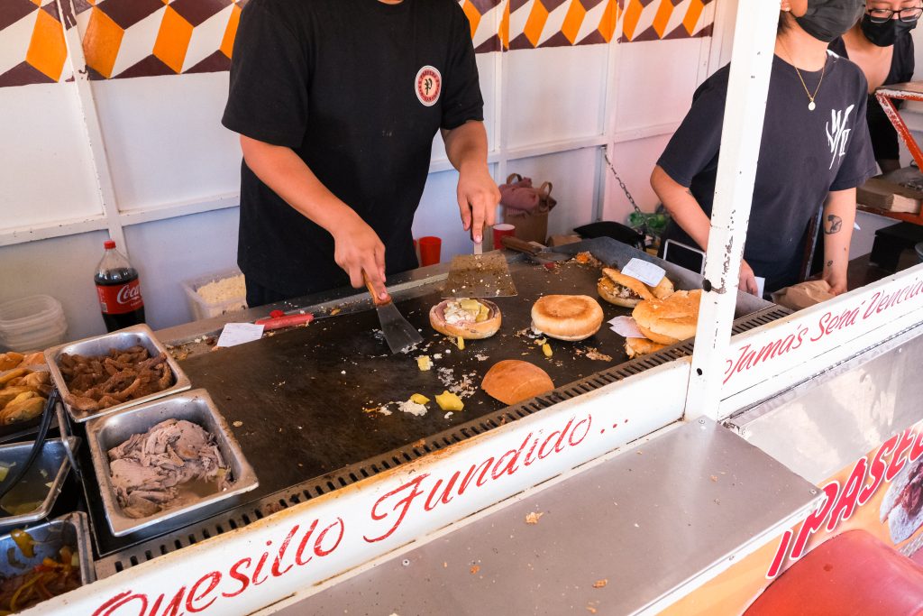 Vendor grilling sandwiches with ingredients like meat and cheese at a food stall.