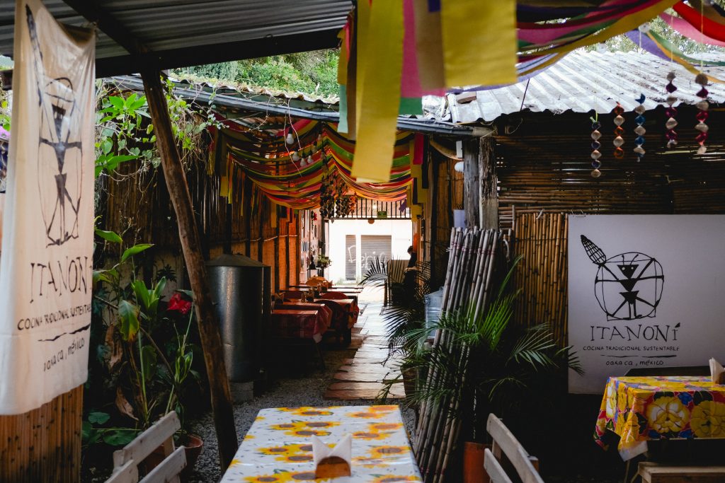 Outdoor cafe with colorful streamers, bamboo walls, and Itanoni signs on fabric banners.