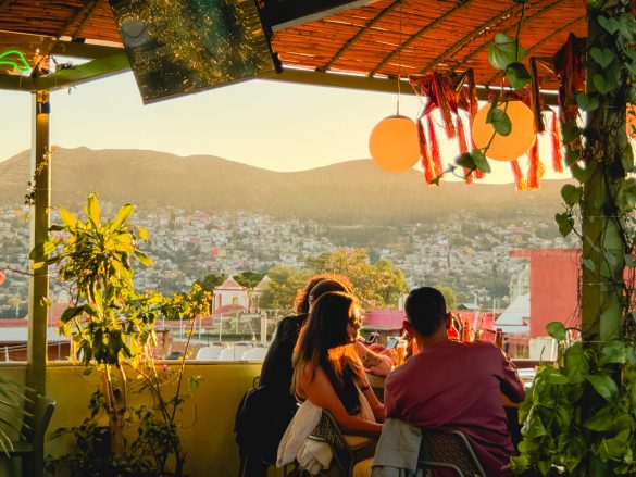 Four people sit at a rooftop bar at sunset, overlooking city buildings and hills capturing the vibrant atmosphere found at the best bars in Oaxaca.