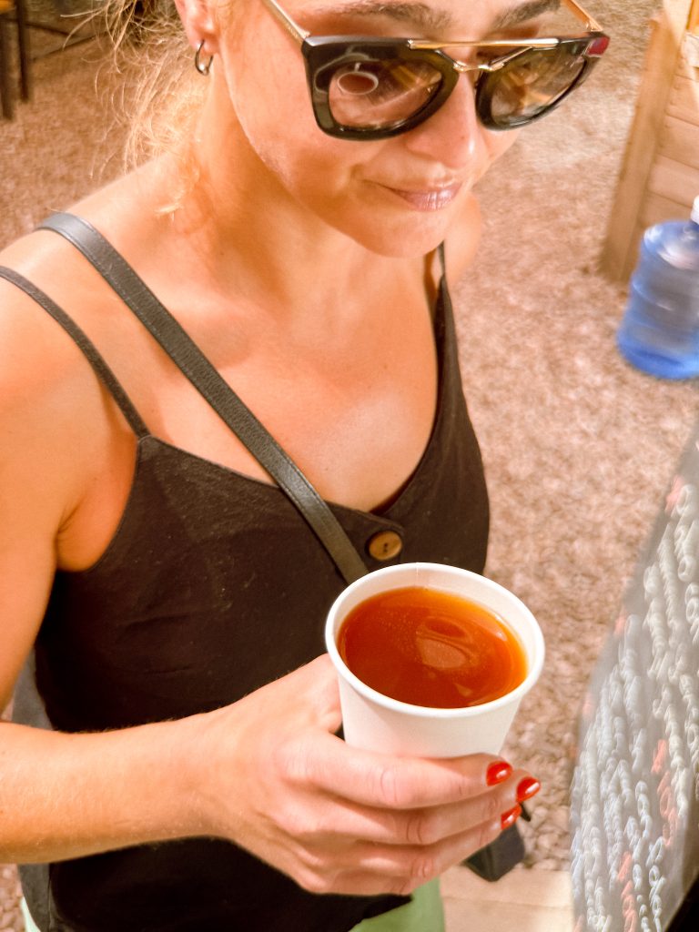 Woman in sunglasses holding a cup of tea or coffee, possibly savoring one of the signature drinks in Oaxaca, wearing a black tank top and red nail polish.