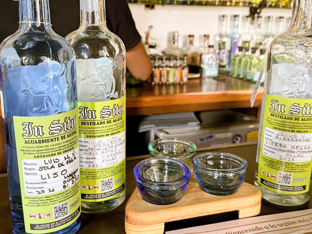 Three brightly labeled mezcal bottles and three shot glasses sit on the bar of In Situ in Oaxaca.
