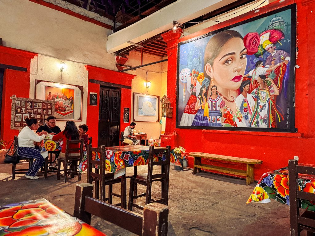 An indoor courtyard filled with tables with colourful tablecloths and red painted walls adorned with Mexican artworks.