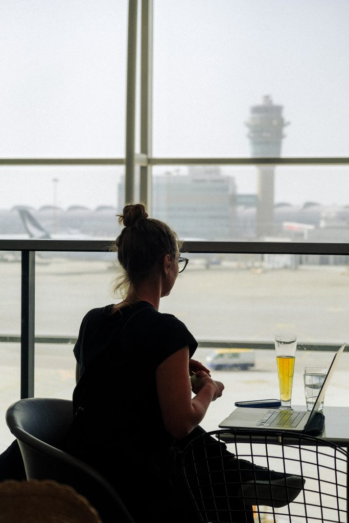 Sofia sits at an airport lounge - with free access with her Amex Platinum card - with a laptop and drink, looking out at the runway.