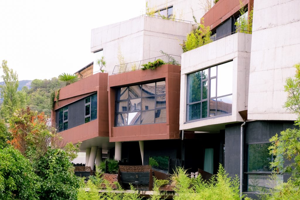 Modern, angular hotel building with large windows, surrounded by greenery and plants.