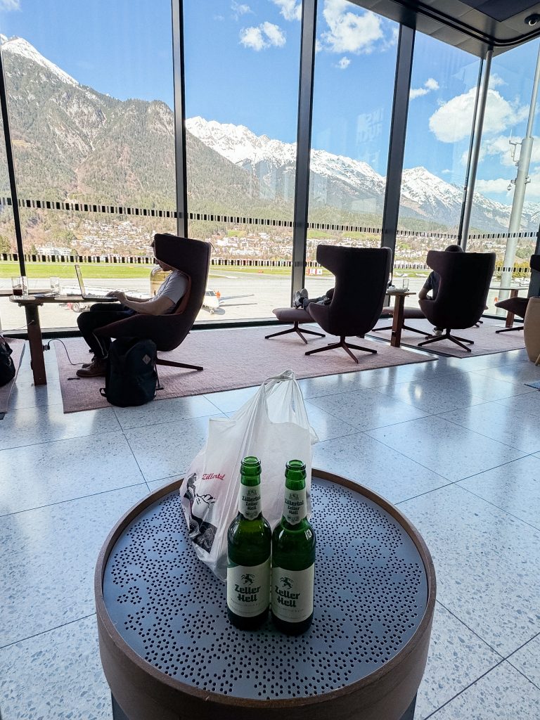 Two beer bottles on a table by airport lounge windows with mountains visible in the background. Another perk of the Amex Platinum card.