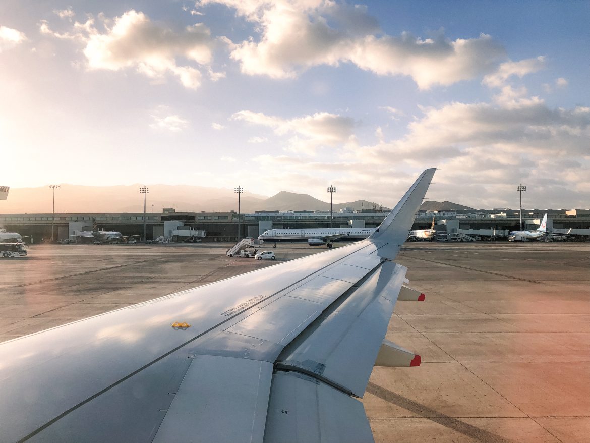 View from an airplane window showing the wing and airport terminal under a partly cloudy sky.
