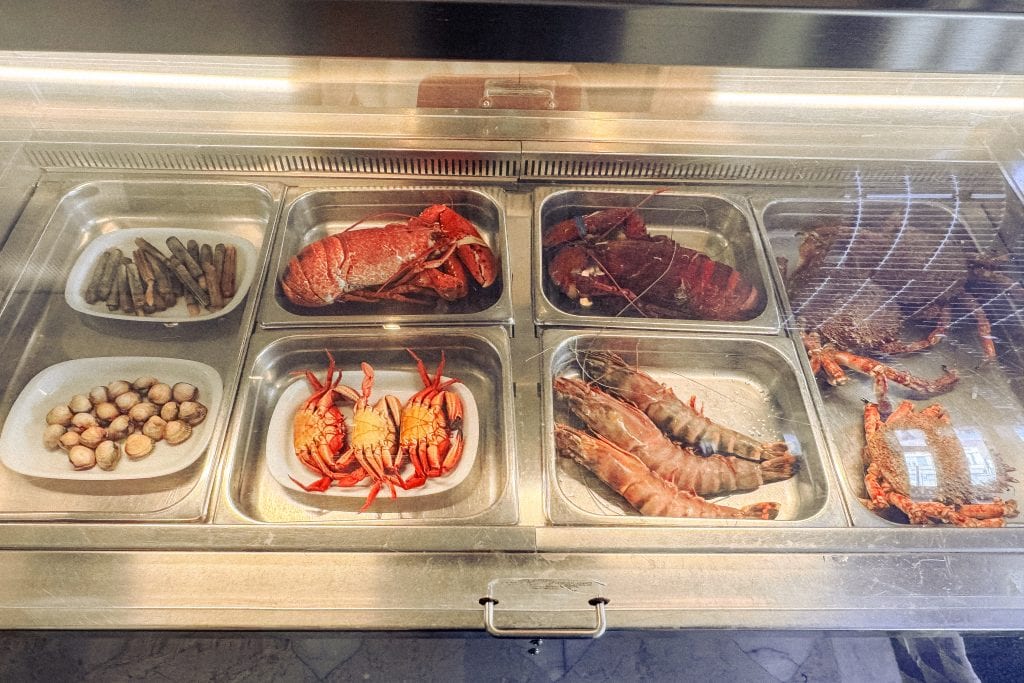 A display case with various seafood including lobster, prawns, crabs, clams, and razor clams.
