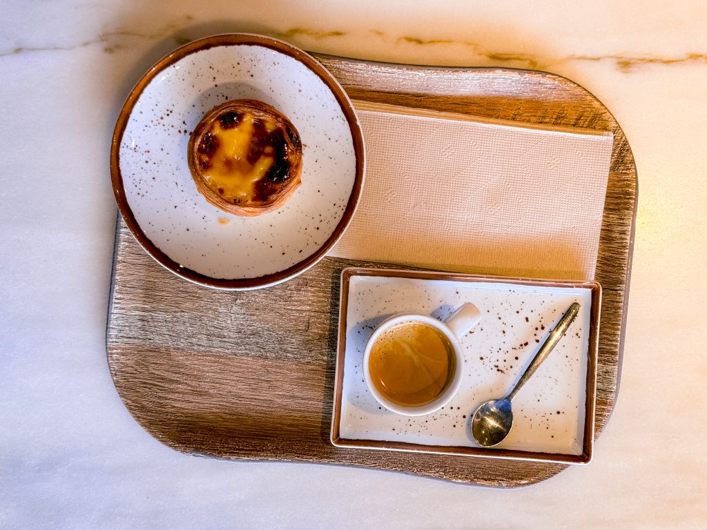 A pastel de nata and an espresso with a spoon, served on a tray with a napkin.