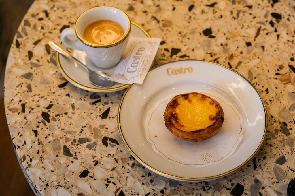 A pastel de nata on a dish with Castro written on, next to an espresso.