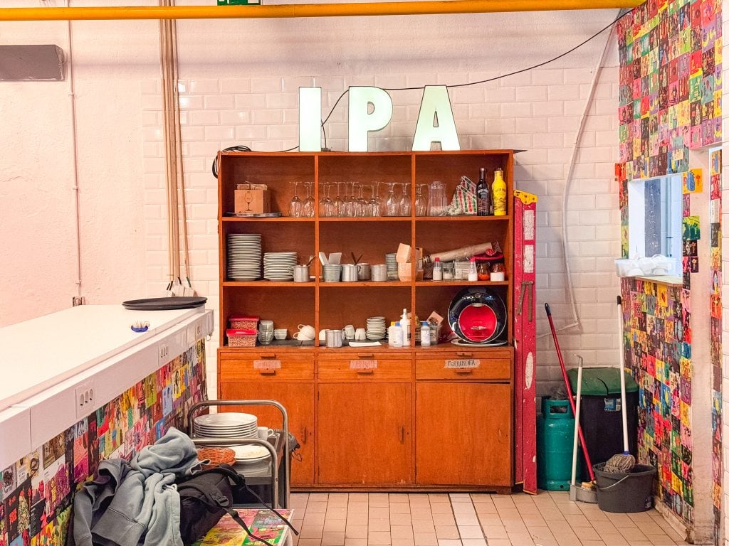 Wooden kitchen cabinet with dishes, utensils, and large IPA letters on top against a tiled wall.