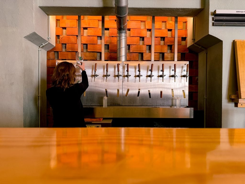 Person pours a craft beer from a row of beer taps at Fermentage, our favourite brewery in Lisbon, with a warm, modern interior design.