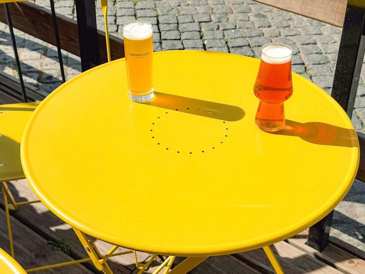 Two glasses of Lisbon's best craft beer on a round yellow table outside, with sunlight casting shadows.