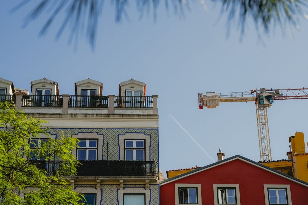 Colorful buildings and a construction crane under a clear blue sky, with tree branches framing the scene.
