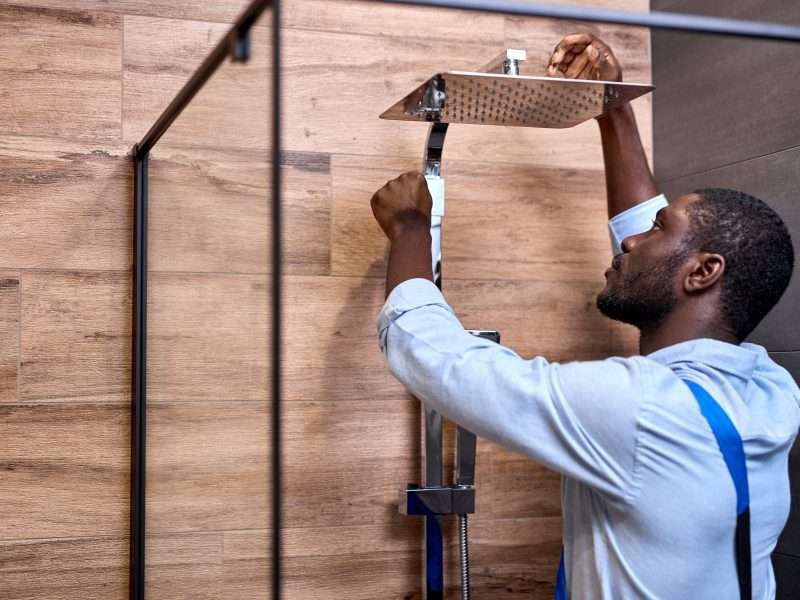 Black Professional handyman working in shower bath indoors, side view portrait