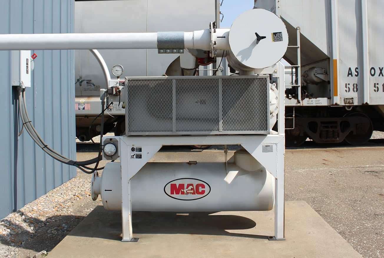 Industrial air compressor outside a building, featuring prominent branding and connected to overhead pipes.