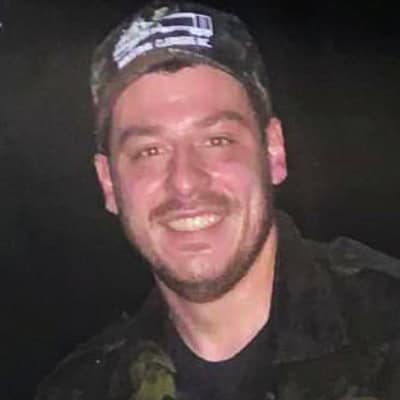 A man in a camouflage jacket smiles for the camera.