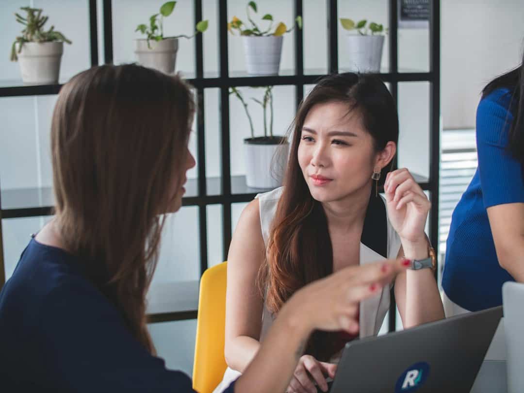 兩位東方女性在桌前討論合作，一人傾聽另一人的意見