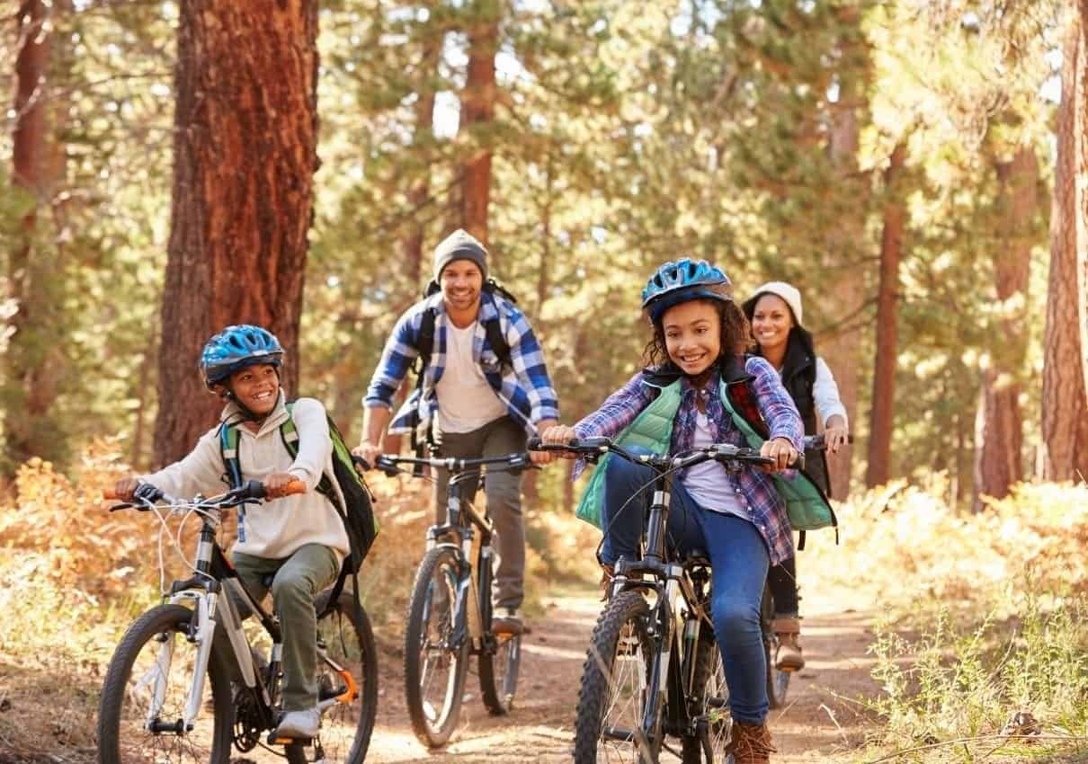Family with two adults and two children biking on a sunny forest trail