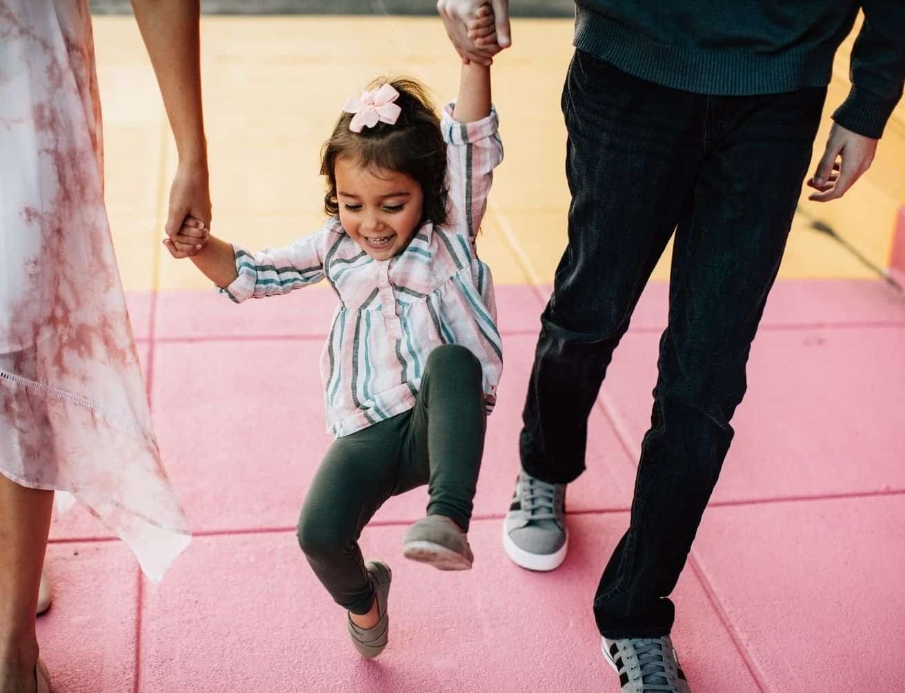 Smiling young girl swinging between her parents while walking outdoors