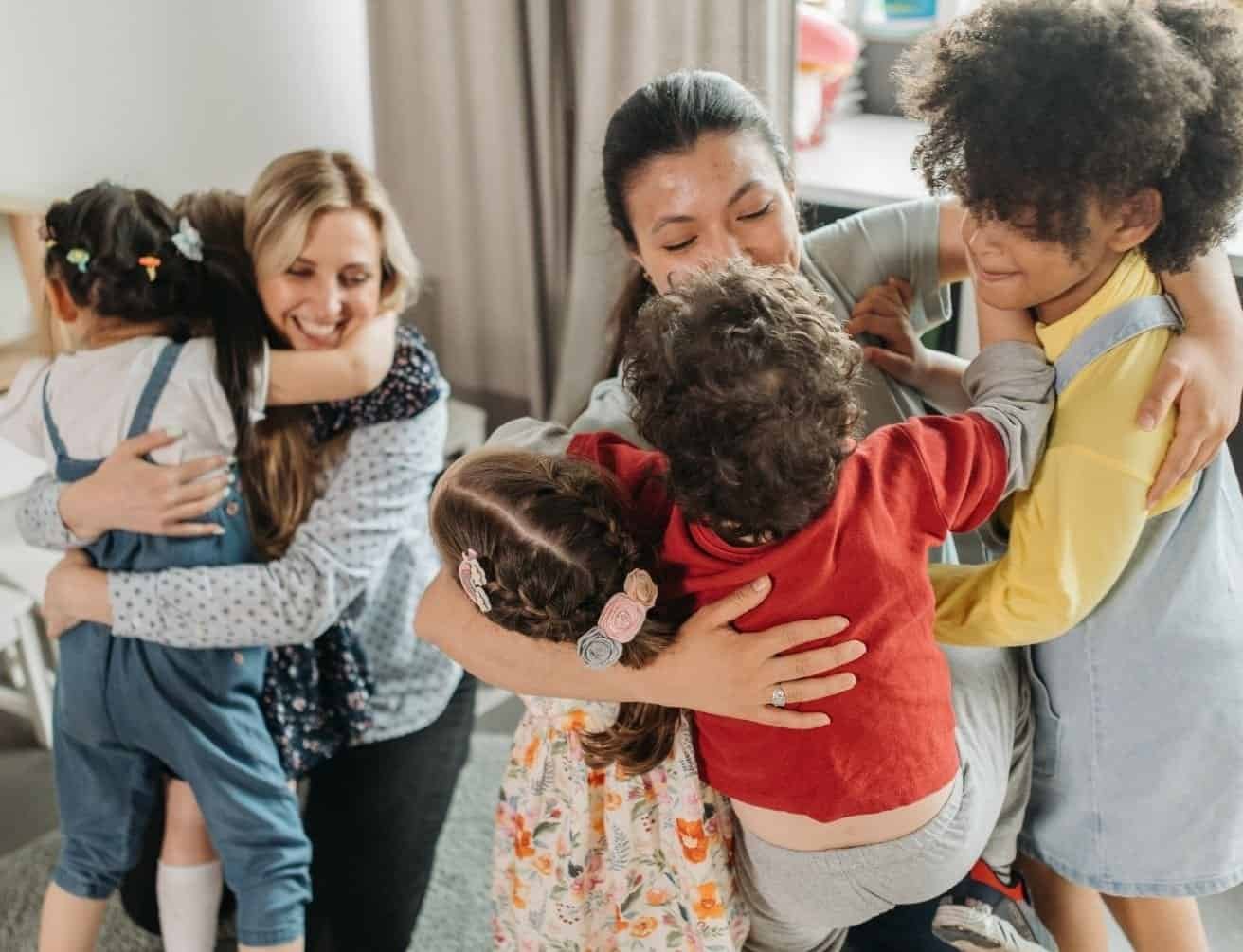 Happy children hugging their female caregivers in a bright, inviting room.