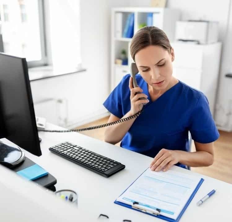 Medical professional in blue scrubs talking on phone and looking at documents