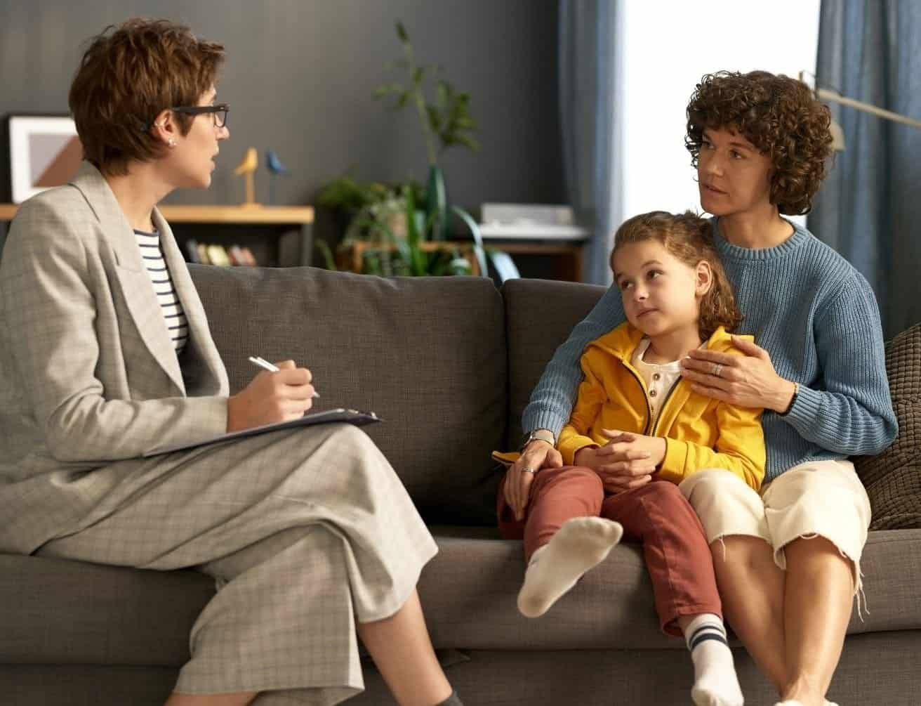 A professional taking notes while a parent and child sit on a sofa