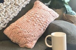 Soft pink knitted pillow on a gray sofa with a white mug nearby.