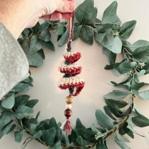 Handmade yarn ornament with wooden beads, hanging on a eucalyptus wreath.