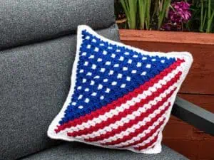 Crochet pillow featuring a vibrant American flag pattern in red, white, and blue, placed on a modern.