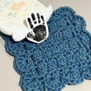 Handmade blue crochet blanket with a baby diaper and a handprint card.