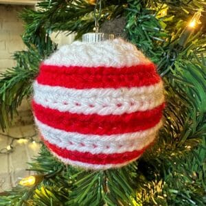 Festive red and white striped knitted Christmas ornament hanging on a decorated tree.