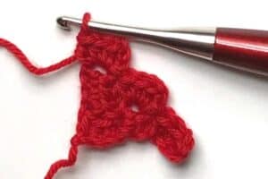 Crochet red stocking ornament with crochet hook for holiday decoration.