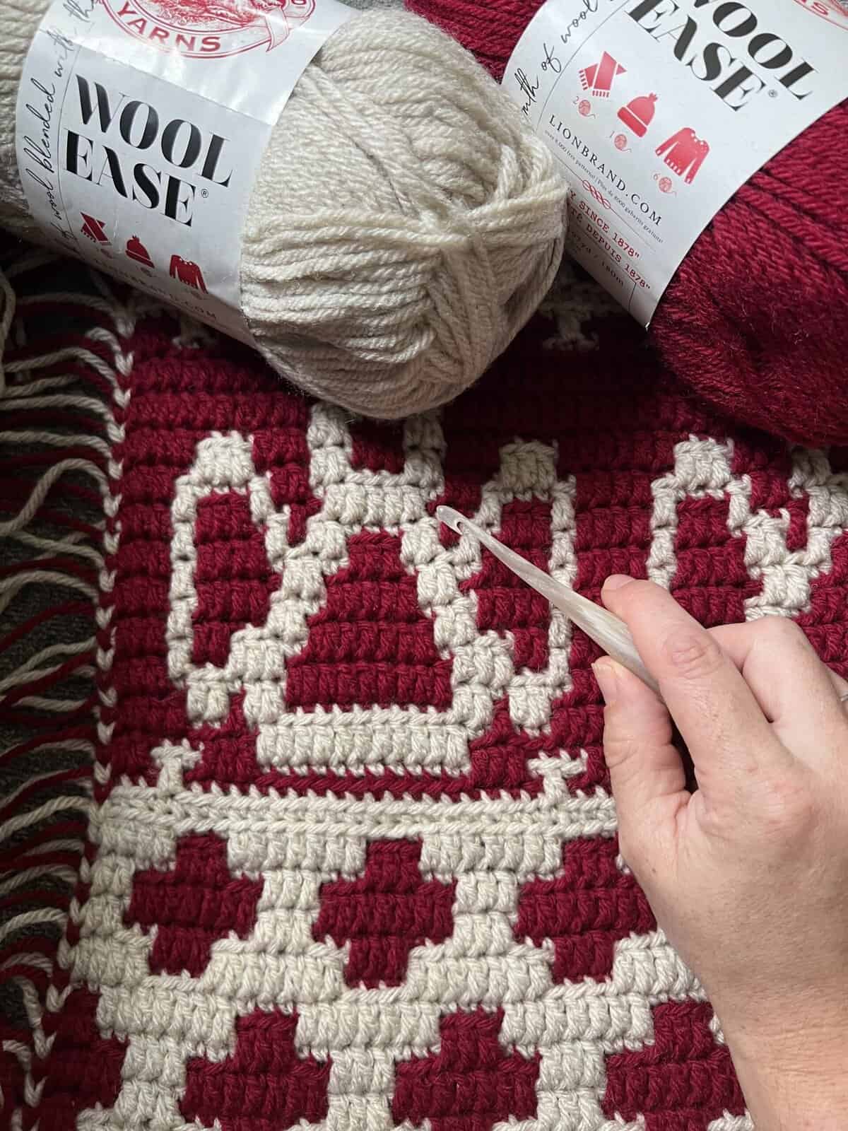 Hand crocheting a Nordic winter afghan with red and cream yarns, showcasing intricate mosaic crochet.