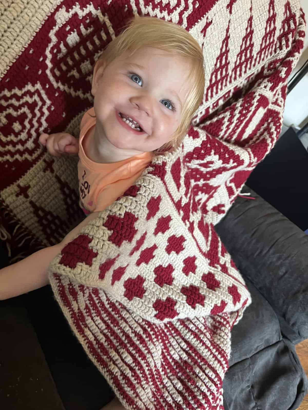 Beautiful child with a joyful smile on a red and white crochet mosaic afghan.