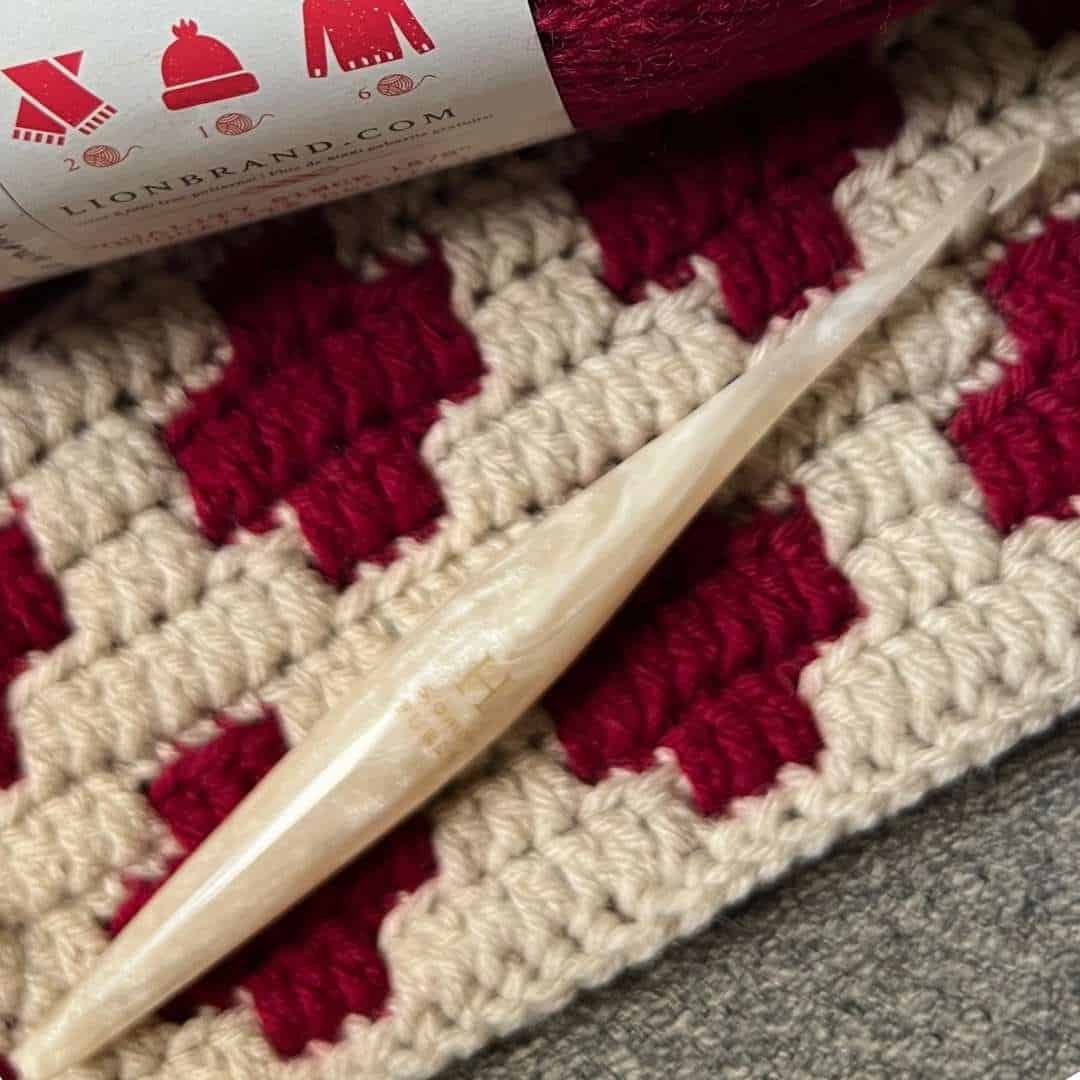Close-up of crochet overlay mosaic pattern using red and cream yarns with a crochet hook.