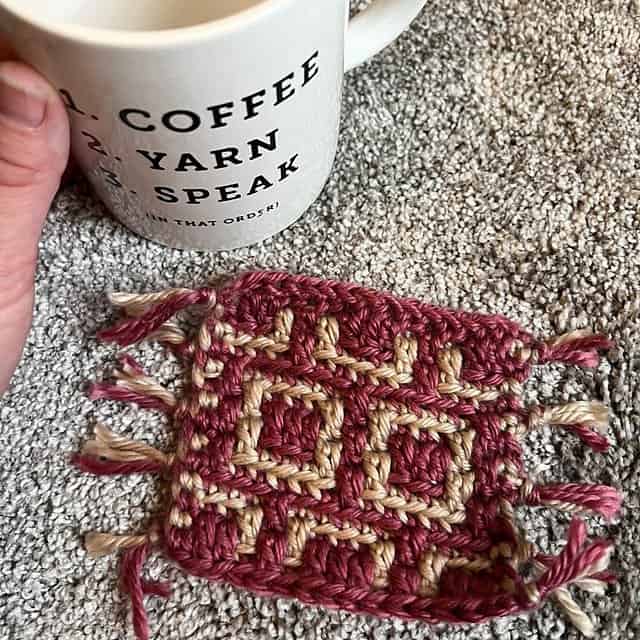 Close-up of a mosaic crochet square with red and beige yarn, on a textured surface.